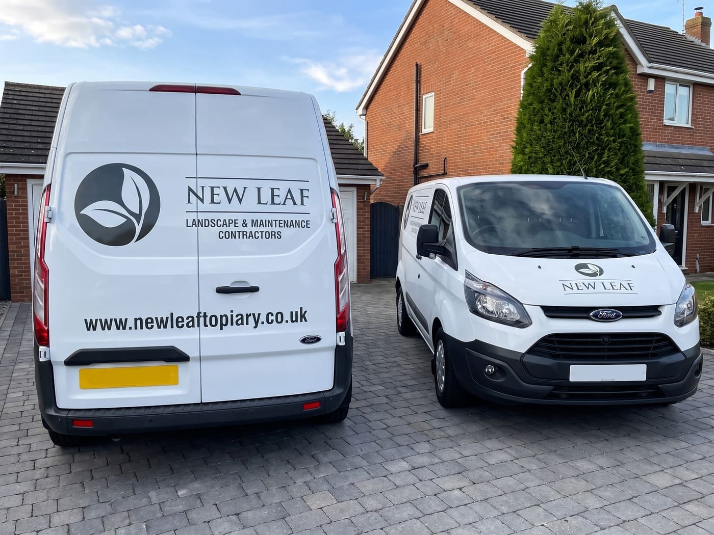 Two white New Leaf vans with the company lettering, parked on a driveway