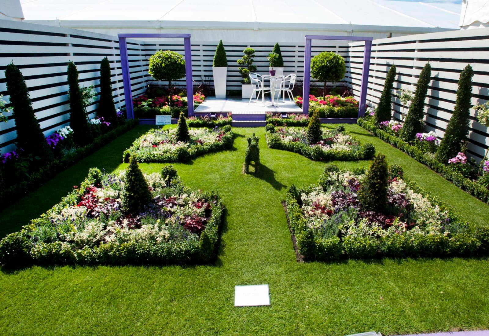 A formal garden of box-edged flower beds, clipped cones, standard trees and lawn
